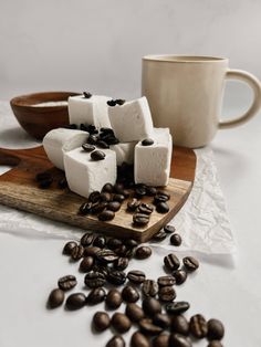 coffee beans and marshmallows on a cutting board next to a cup of coffee