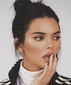 a woman with black nail polish holding her hand up to her mouth and looking at the camera