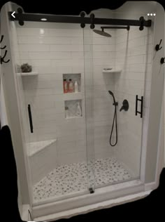 a walk in shower with white tile and black fixtures on the walls, along with shelves