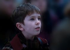 a young boy with blue eyes is looking to the side while standing in front of a crowd