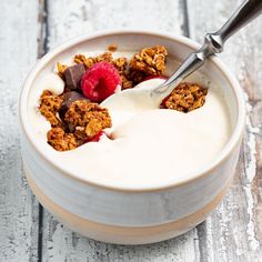 a white bowl filled with granola and raspberries on top of a wooden table