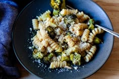 a black plate topped with pasta and broccoli covered in parmesan cheese