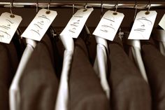 there are four suits with name tags on them hanging from a rack in the closet