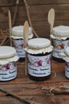 several jars of jam with spoons on a wooden table in front of some sticks