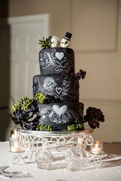 a three tiered cake with skulls and flowers on the top is surrounded by candles