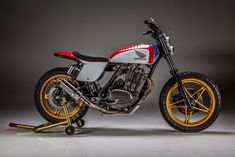 a red, white and blue motorcycle parked on top of a gray floor next to a black wall