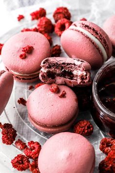 some pink macaroons are on a glass plate with red crumbles around them