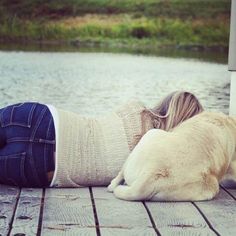 a woman laying on top of a wooden dock next to a brown and white dog