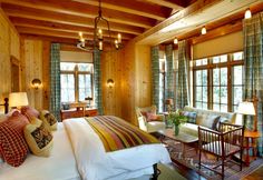 a bedroom with wood paneling and wooden furniture in front of two large windows that look out onto the woods