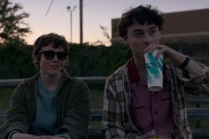 two young men sitting on a bench drinking beverages