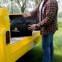 a man standing next to the back of a yellow pickup truck holding a black bag