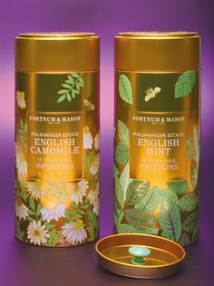 two tins are sitting next to each other on a purple surface with flowers and leaves