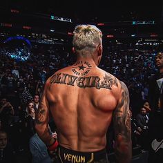 a man with tattoos on his back stands in front of an audience at a sporting event