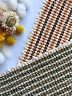 some white and orange flowers sitting on top of a plaid table cloth next to cotton balls