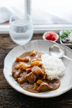 a white plate topped with meat and rice next to a glass of water on a wooden table