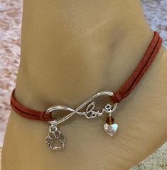 This anklet features an infinity charm with a silhouette paw charm. Attached to the infinity charm is brown leather straps. A brown bead and silver heart  bead dangle from the infinity charm.  This anklet detaches at the back of the anklet with a lobster claw latch and is size adjustable. Comfortable and versatile, it will lend itself to casual or formal events. All items are made in a smoke free environment. *If there is any issue with your anklet, please let me know so I can correct it. Thanks for visiting my shop!👣 Adjustable Anklets For Valentine's Day Gift, Elegant Adjustable Anklets With Heart Charm, Adjustable Heart Metal Anklets, Heart-shaped Anklets For Valentine's Day, Adjustable Heart Charm Anklets, Adjustable Heart-shaped Dainty Anklets, Leather Anklets, Columbia Tn, Beaded Ankle Bracelets