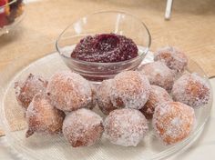 powdered sugar covered doughnuts on a plate next to a bowl of jelly