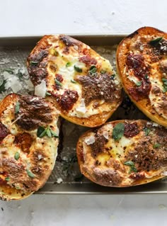 four baked pizzas sitting on top of a baking pan covered in cheese and herbs