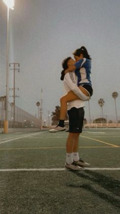 two people embracing each other on a tennis court with lights in the background and palm trees behind them