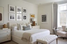 a bedroom with white walls and pictures on the wall above the bed, along with an ottoman