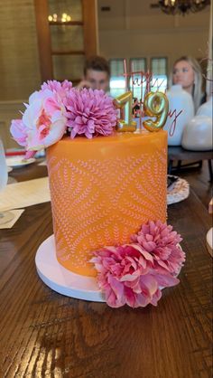 an orange cake with pink flowers and the number ten on it's top is sitting on a wooden table