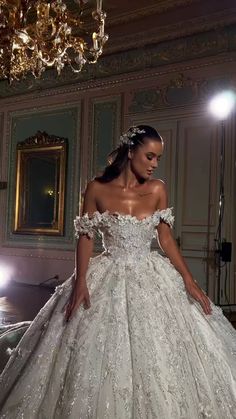 a woman in a white wedding dress is standing near a chandelier