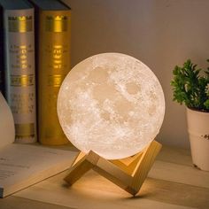 the moon lamp is sitting on top of a wooden stand next to books and plants