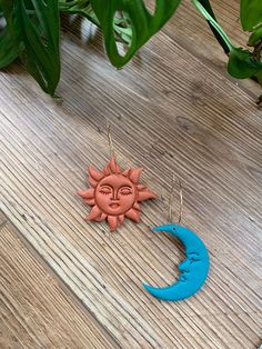 the sun and moon earrings are hanging from hooks on a wooden table next to a potted plant