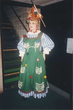 a woman dressed as a clown holding a stick and wearing a green dress with white stripes