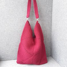 a pink crocheted bag hanging on the wall next to a gray couch with white pillows