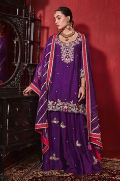 Purple A-line short kurta with intricate neckline embroidery and scalloped embroidered hem. Comes with an embroidered sharara and gota embellished dupatta.
Components: 3
Pattern: Embroidered
Type Of Work: Floral Patterns
Neckline: Round
Sleeve Type: Straight Three Quarter
Fabric: Dupion Silk and Organza
Color: Purple
Other Details: 
Scalloped hem kurta
Floral buttis
Contrast border dupatta
Occasion: Wedding - Aza Fashions Purple Anarkali, Mehndi Outfit, Embroidered Sharara, Neckline Embroidery, Kurta Sharara Set, Gown Pictures, Womens Pants Design, Kurta Sharara, Organza Gowns