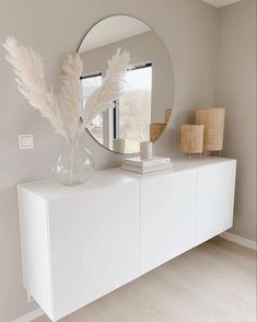 a white dresser with a round mirror on the top and two vases in front of it