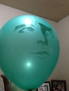 a person holding up a green balloon with a drawing on it's face in the air