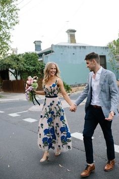 a man and woman holding hands while walking down the street with flowers in their hand