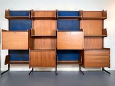 a wooden shelf with blue shelves and drawers on wheels in front of a white wall