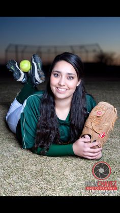 a woman laying on the ground holding a catchers mitt and two balls in her hand