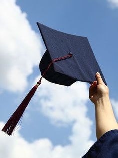 a graduation cap being held up in the air by someone's hand, against a blue sky with white clouds