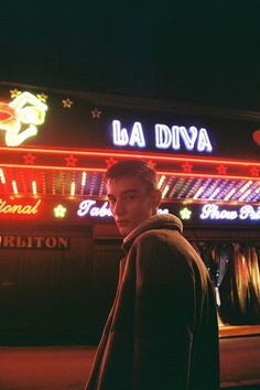 a man standing in front of a neon lit building with the name la diva on it