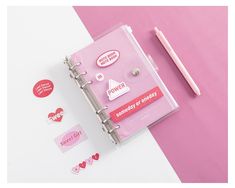 a pink binder with some stickers and a pen on the table next to it