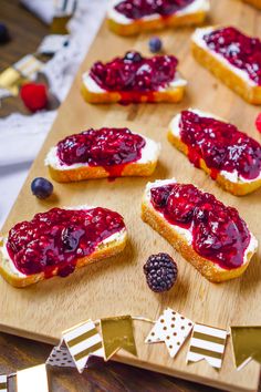 several pieces of bread with jam and berries on them sitting on a wooden cutting board