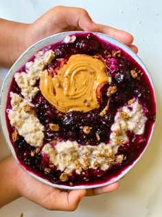 two hands holding a bowl of oatmeal with peanut butter and blueberries