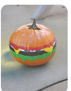 an orange pumpkin with a hamburger painted on it's side sitting on the ground