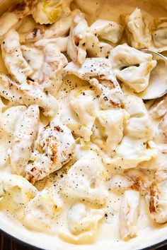 a skillet filled with chicken and dumplings covered in cream sauce on top of a wooden table