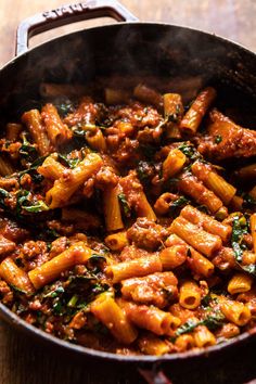 pasta with meat and spinach in a pan on a wooden counter top, ready to be eaten