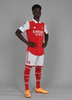 a soccer player poses for the camera in his red and white uniform with yellow socks