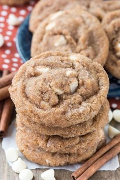 several cookies stacked on top of each other with cinnamon sticks in the foreground and white chocolate sprinkles around them