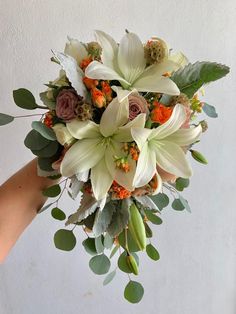 a bridal bouquet with white lilies and greenery is held by a woman's hand