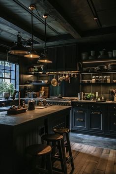 a kitchen with black cabinets and wooden floors is lit by pendant lights above the island