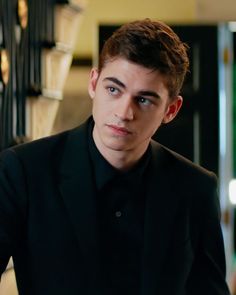 a young man in a black suit looks at the camera