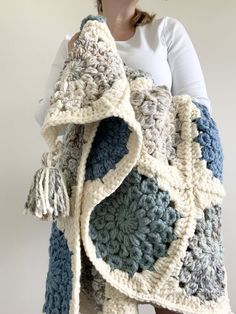 a woman is holding up a crocheted blanket